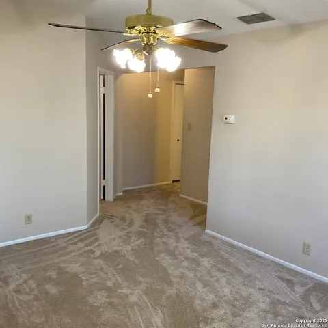 an empty room with a chandelier fan and kitchen view