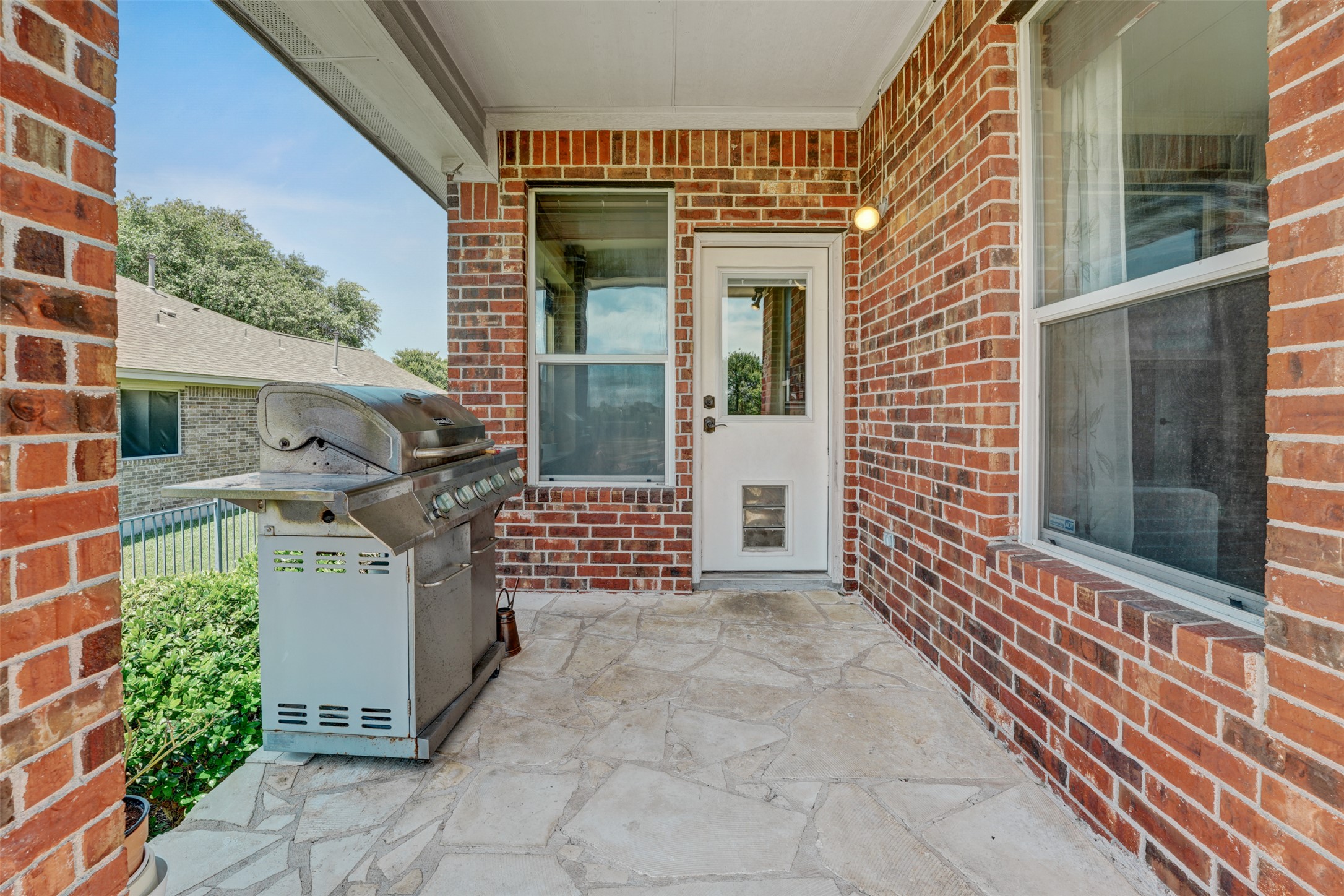 2521 Amen Corner Road Pflugerville, TX 78660 - Photo 35 of 40 Covered patio area featuring flagstone flooring, red brick exterior walls, and a white exterior door with a lower glass panel