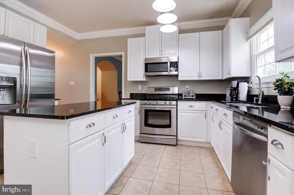 a kitchen with stainless steel appliances granite countertop white cabinets a sink a stove and a refrigerator