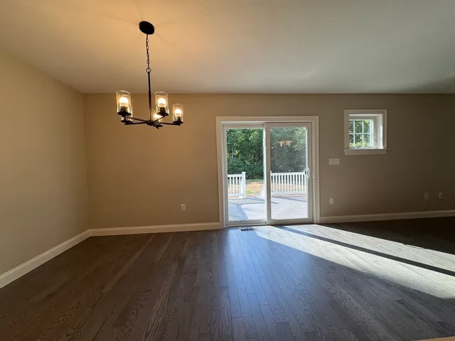 a view of empty room with wooden floor and kitchen