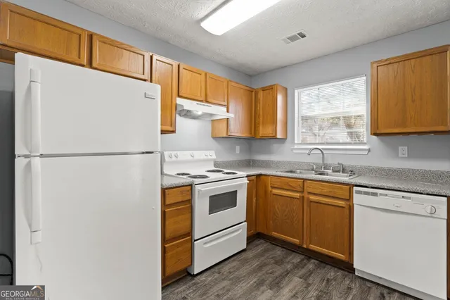 a kitchen with stainless steel appliances granite countertop a refrigerator a sink dishwasher a stove with white cabinets and wooden floor