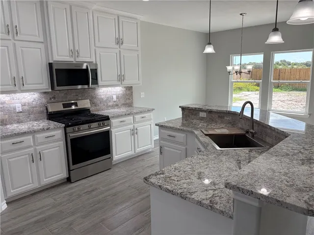 a kitchen with stainless steel appliances granite countertop a stove a microwave and a white cabinets