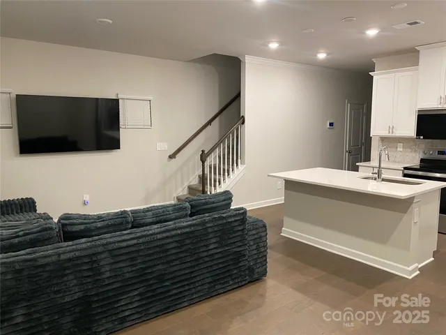 a view of living room kitchen with stainless steel appliances wooden floor and flat screen tv
