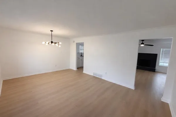 a view of empty room with wooden floor and kitchen