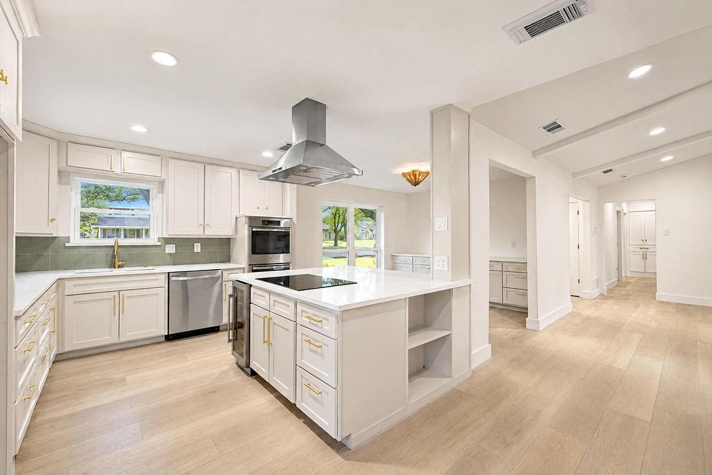 1904 Apollo Road Richardson, TX 75081 - Photo 11 of 40 Kitchen featuring light wood-finish flooring, white cabinetry with gold-finish hardware, stainless steel appliances, a center island with built-in cooktop, and recessed lighting