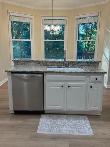 a kitchen with granite countertop a stove a sink and white cabinets with wooden floor