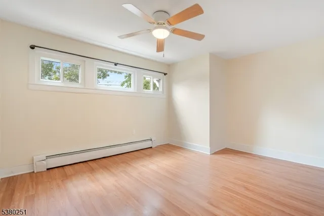 an empty room with wooden floor ceiling fan and windows