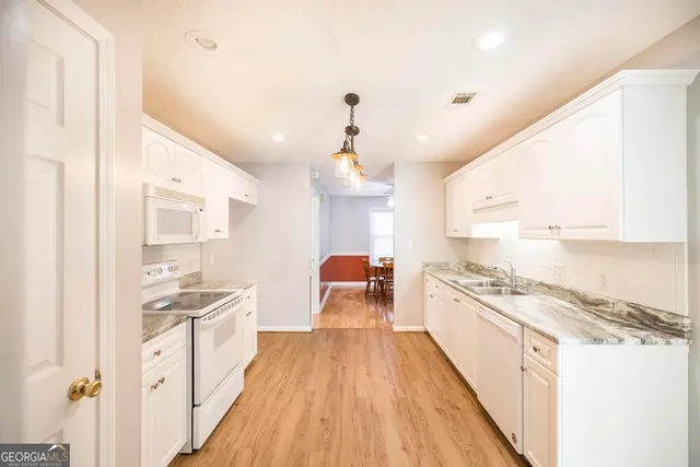 a large kitchen with kitchen island a stove a sink dishwasher and white cabinets with wooden floor