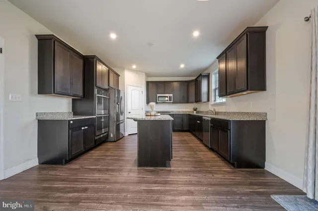 a large kitchen with stainless steel appliances granite countertop a stove top oven a sink and dishwasher with wooden floor