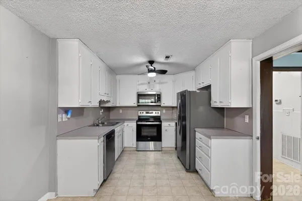 a kitchen with kitchen island granite countertop a refrigerator oven a sink dishwasher and white cabinets with wooden floor