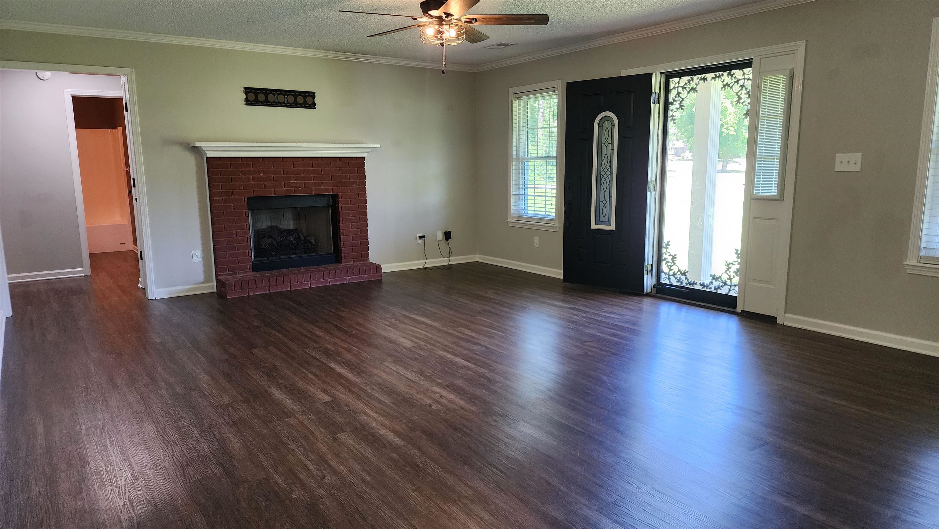 445 Caldwell Road Ripley, TN 38063 - Photo 3 of 14 Unfurnished living room featuring ceiling fan, dark wood-type flooring, baseboards, a fireplace, and crown molding