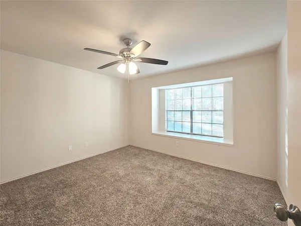 an empty room with chandelier fan and windows