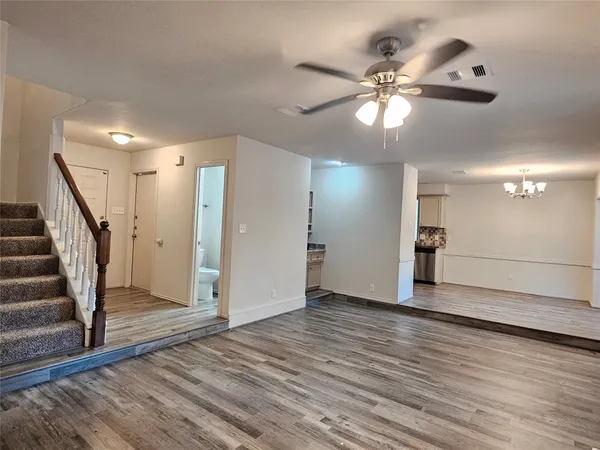 a view of an empty room with wooden floor and a ceiling fan