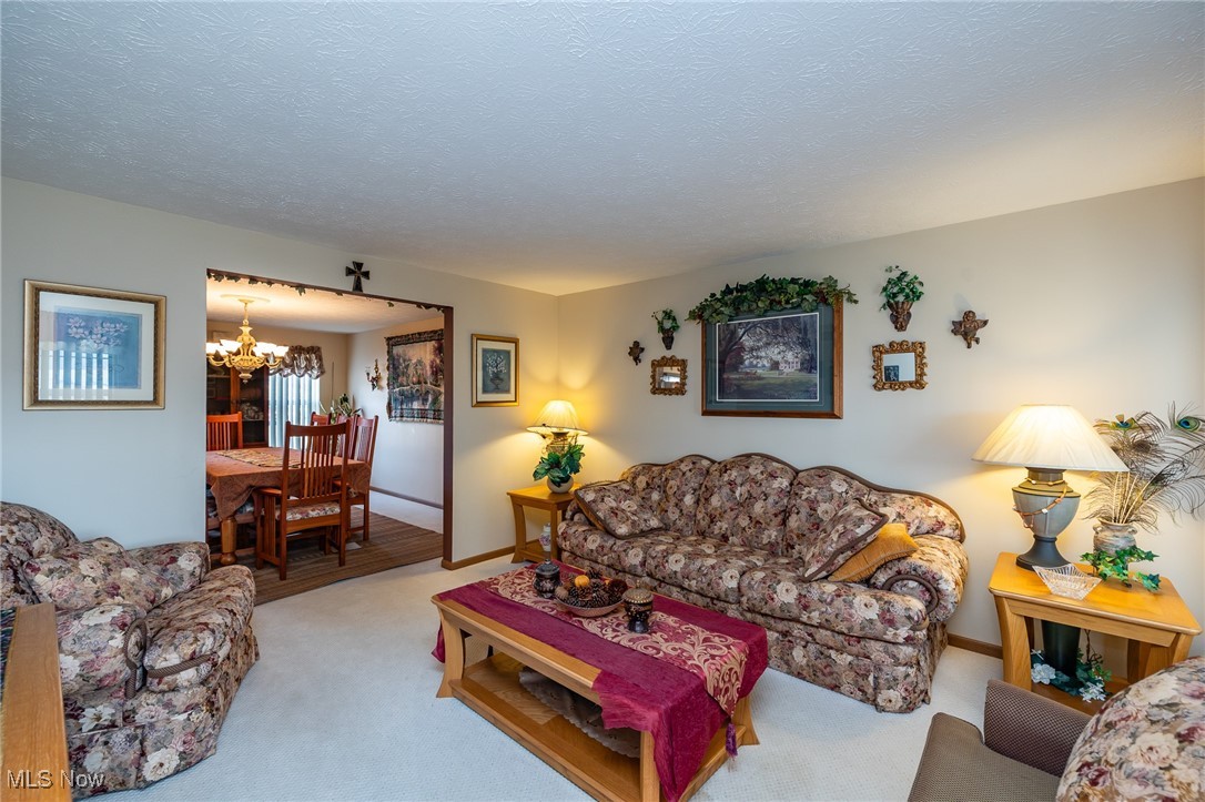 12181 Williams Road Homerville, OH 44235 - Photo 14 of 49 Carpeted living room with a textured ceiling and an inviting chandelier