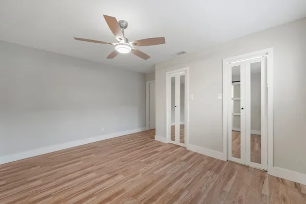 an empty room with wooden floor a ceiling fan and windows
