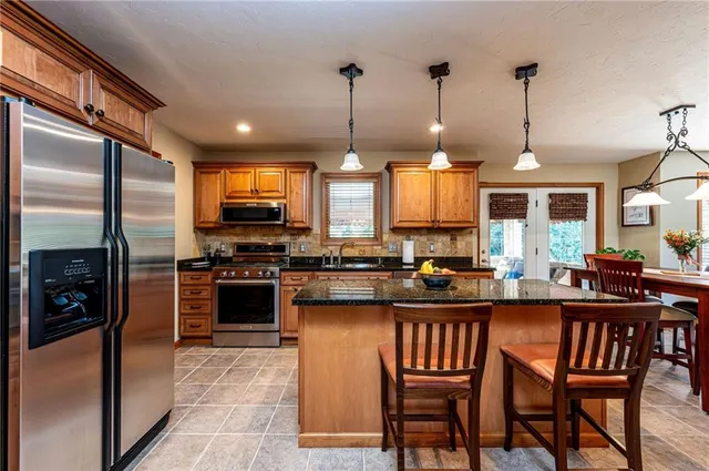 a kitchen with stainless steel appliances granite countertop a stove top oven a sink a dining table and chairs