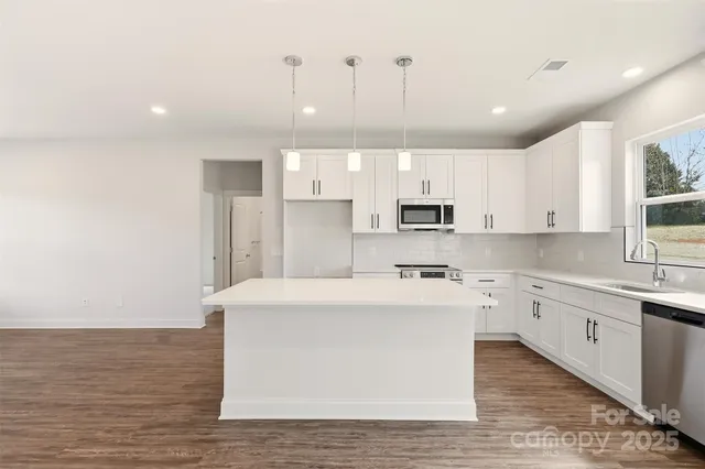 a large kitchen with stainless steel appliances granite countertop a white stove top oven a sink dishwasher and a refrigerator with wooden floor