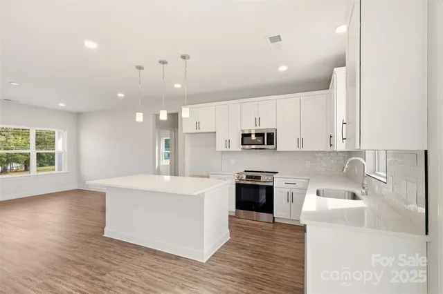 a large kitchen with stainless steel appliances kitchen island granite countertop a stove a sink a refrigerator and white cabinets with wooden floor