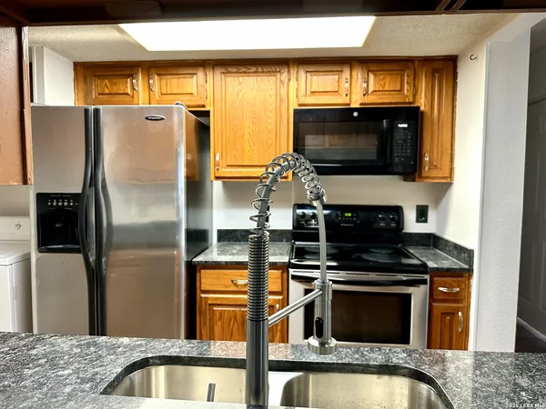 a kitchen with stainless steel appliances granite countertop a refrigerator a stove and a sink with wooden floor