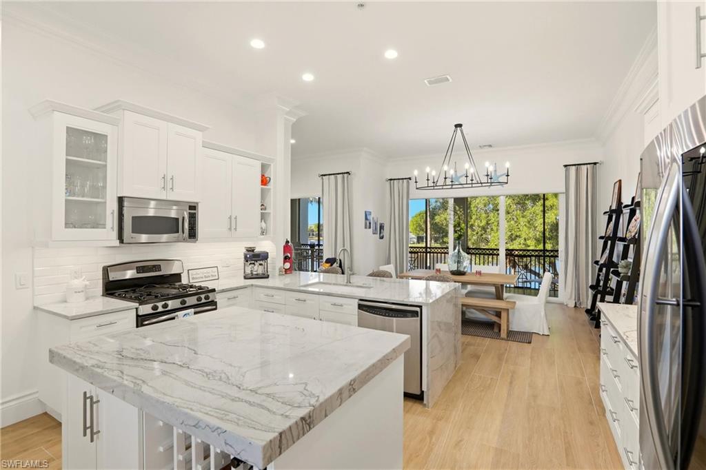 9263 Museo Circle, Unit 202 Naples, FL 34114 - Photo 12 of 50 a kitchen with stainless steel appliances granite countertop a stove top oven a sink dishwasher a dining table and chairs with wooden floor