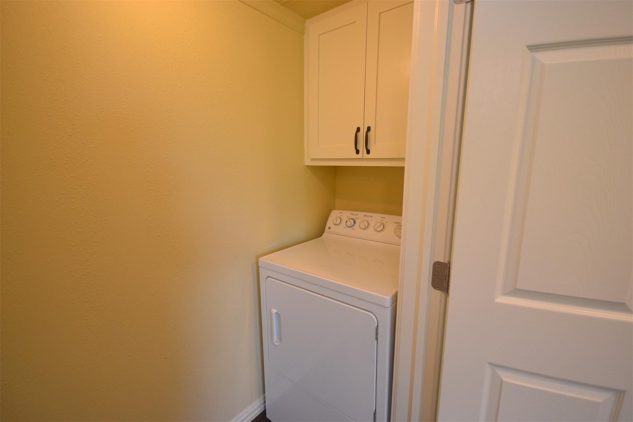 12652 Calvary Road Willis, TX 77318 - Photo 15 of 20 Compact laundry area featuring a sleek dryer with overhead cabinetry for convenient storage.