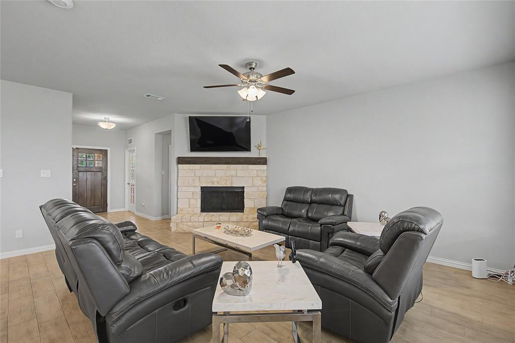 185 Chester Road Springtown, TX 76082 - Photo 14 of 40 Living area featuring wood-finish flooring, a stone-clad fireplace with a wood mantel, a ceiling fan with integrated lighting, and neutral wall tones