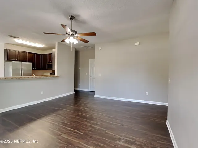 a view of an empty room with kitchen a ceiling fan and wooden floor