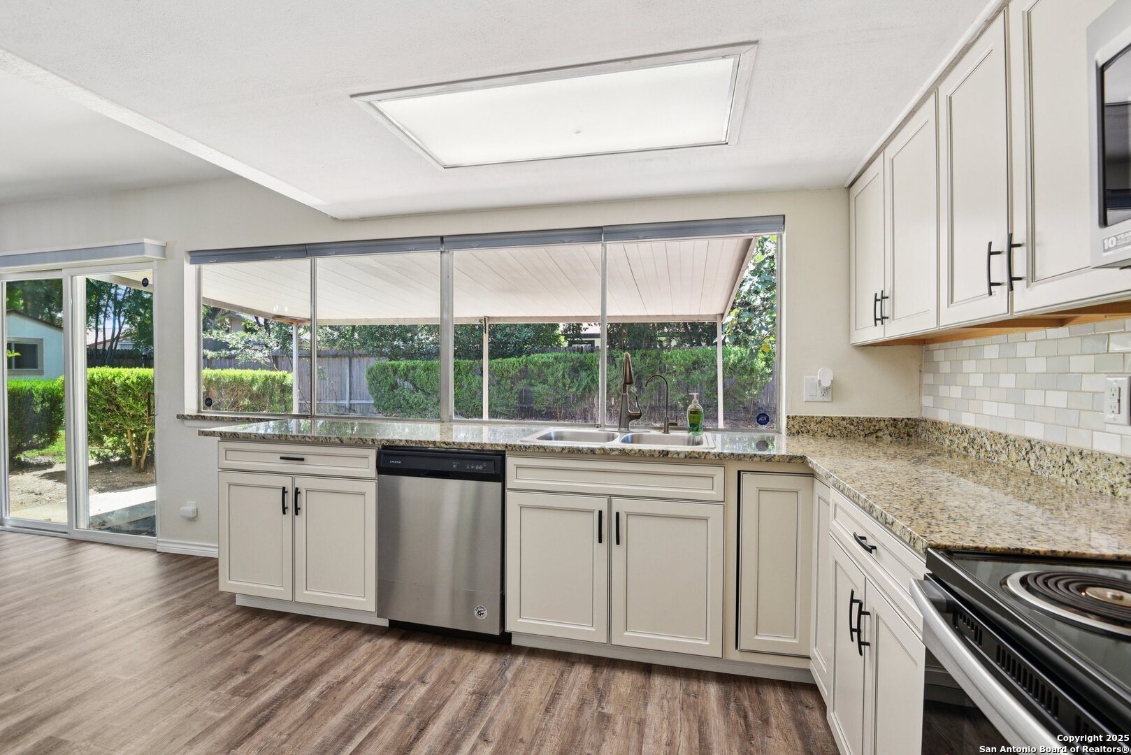 6630 Spring Hollow Street San Antonio, TX 78249 - Photo 20 of 40 a kitchen with a stove a sink and white cabinets with wooden floor next to windows