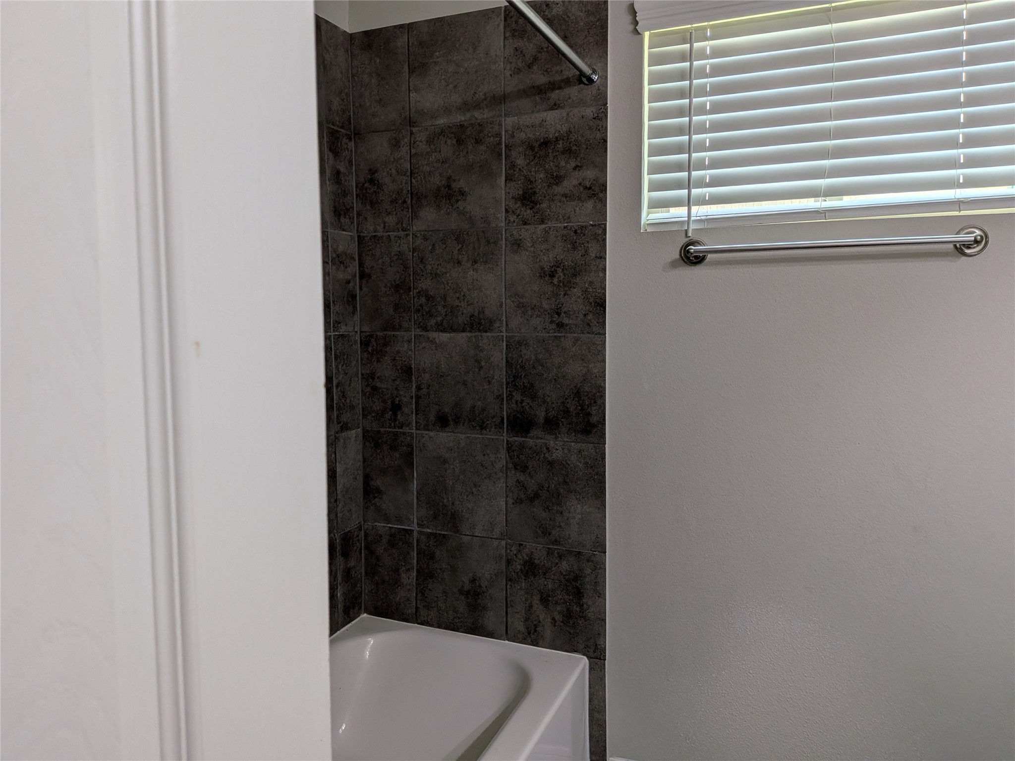 15730 Joe Dimaggio Street Splendora, TX 77372 - Photo 15 of 20 This bathroom features a sleek, modern design with dark tiled walls, a white bathtub, and a window with blinds for natural light and privacy.