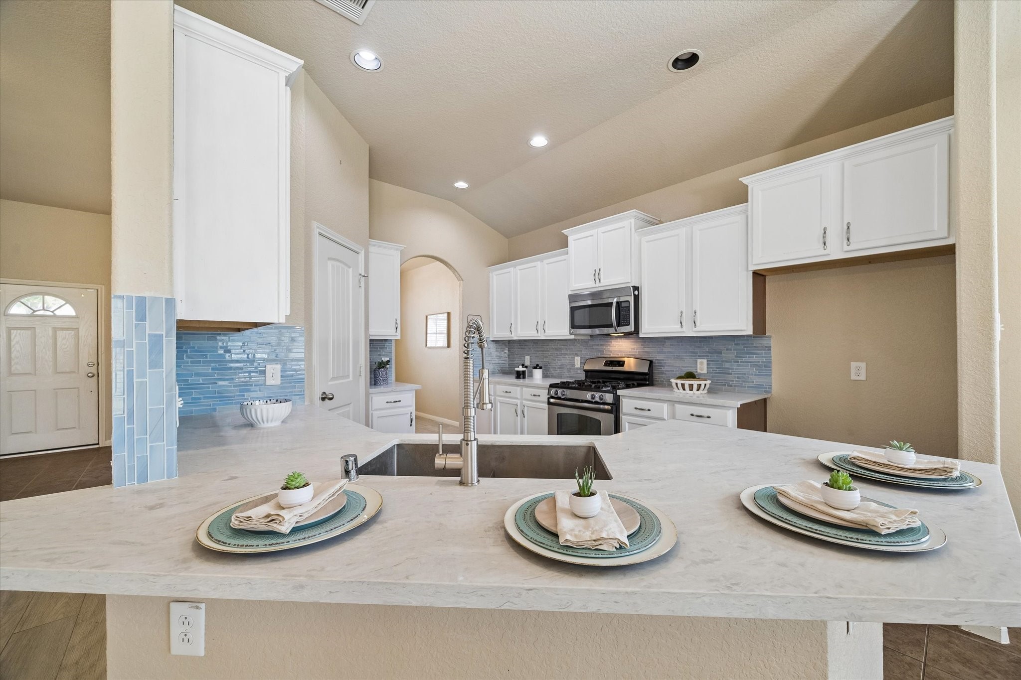 7806 Summer Night Lane Rosenberg, TX 77469 - Photo 9 of 23 The kitchen workspace features a stainless steel undermount sink with a gooseneck faucet, a blue subway tile backsplash, and white cabinetry.