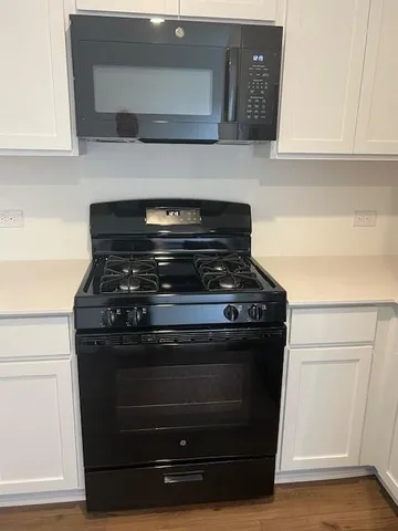 a kitchen with a sink a stove top oven and white wooden cabinets