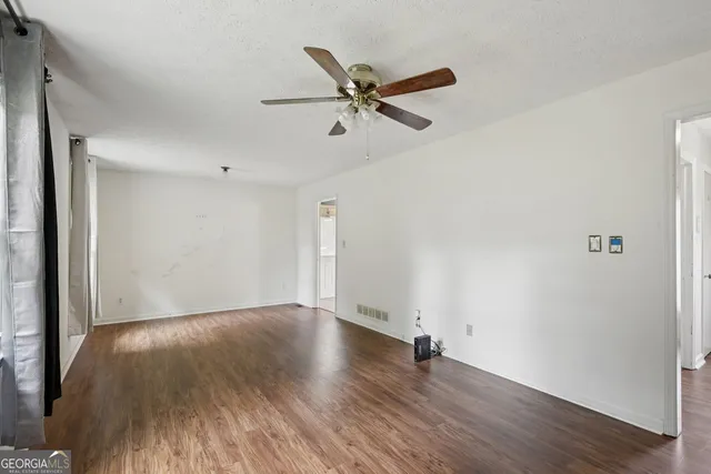 a view of an empty room with wooden floor and a ceiling fan