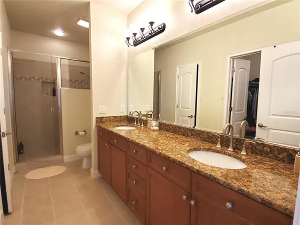 a bathroom with a granite countertop double vanity sink a mirror and a shower