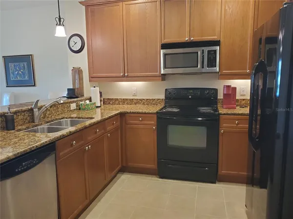 a kitchen with stainless steel appliances granite countertop a refrigerator a stove a sink and dishwasher with wooden cabinets