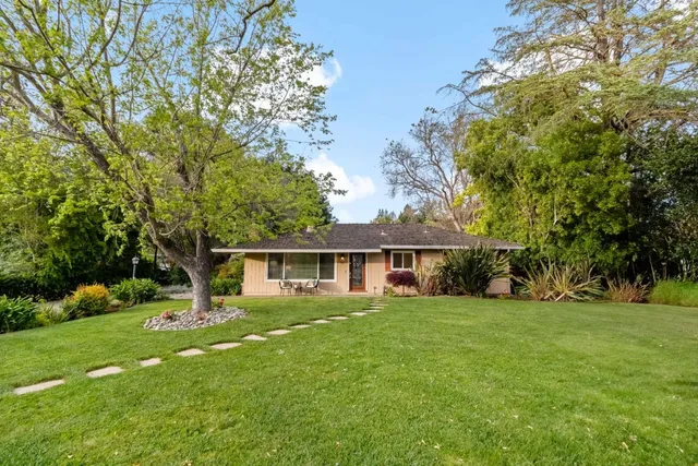a view of a house next to a big yard and large trees