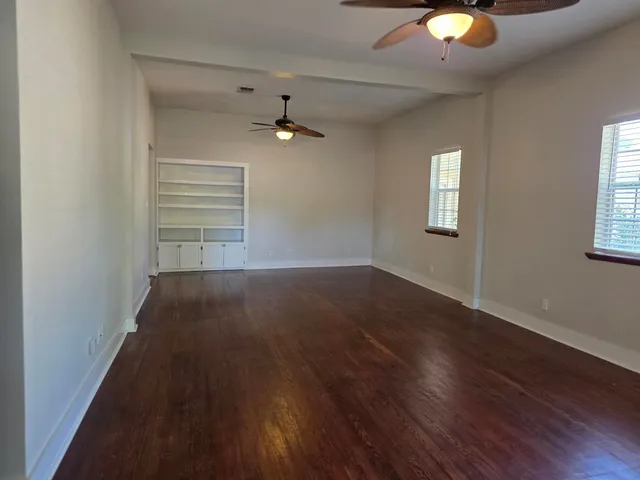 an empty room with wooden floor fan and windows