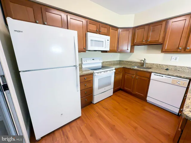 a white refrigerator freezer sitting inside of a kitchen with stainless steel appliances granite countertop wooden cabinets a stove a sink and a refrigerator