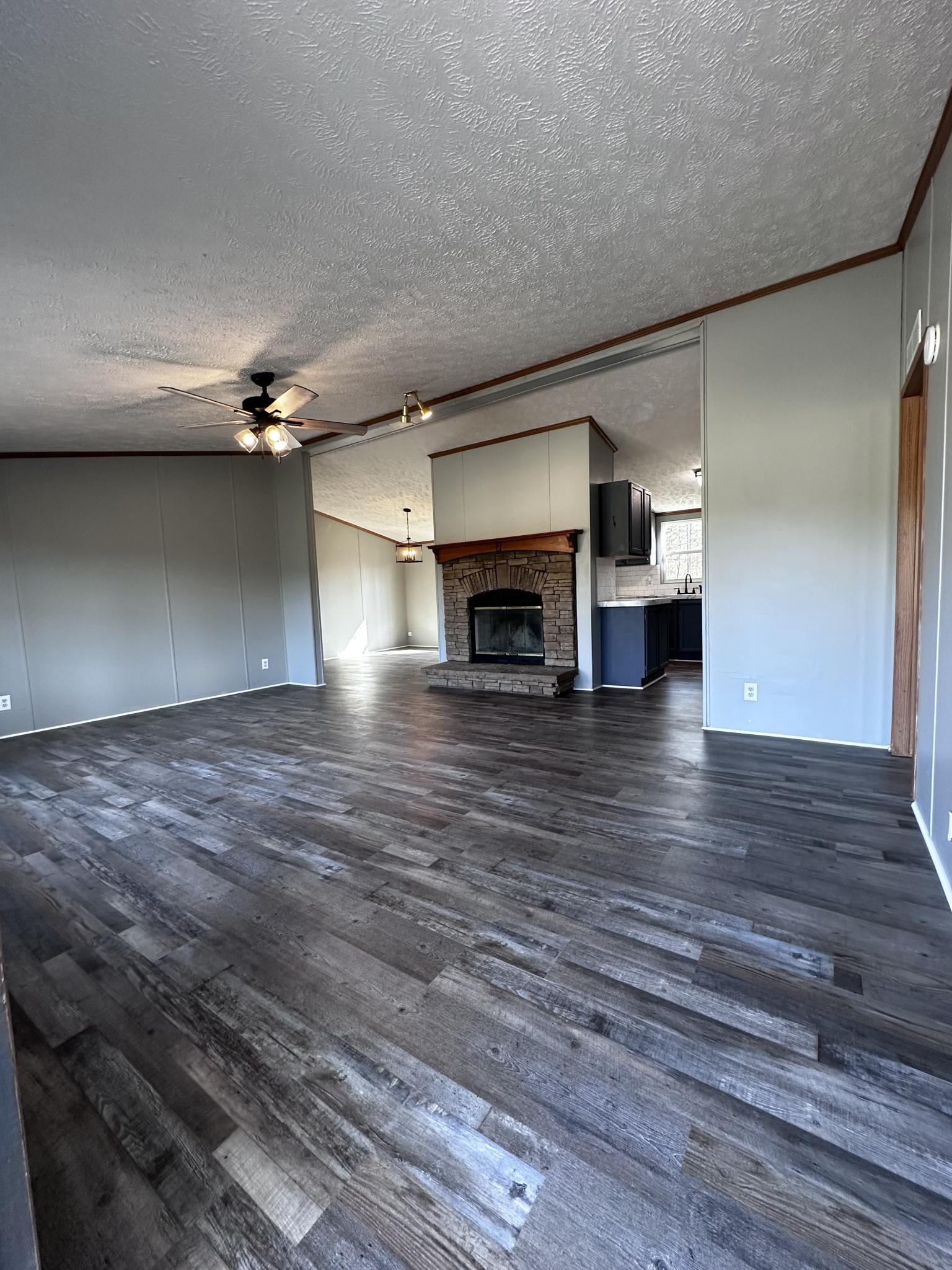 270 Webb Mill Bridge Road Hornsby, TN 38044 - Photo 3 of 19 Unfurnished living room with crown molding, a fireplace, a textured ceiling, ceiling fan, and dark wood-style flooring