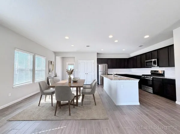 a kitchen with stainless steel appliances granite countertop a stove a sink a microwave refrigerator and a dining table with wooden floor