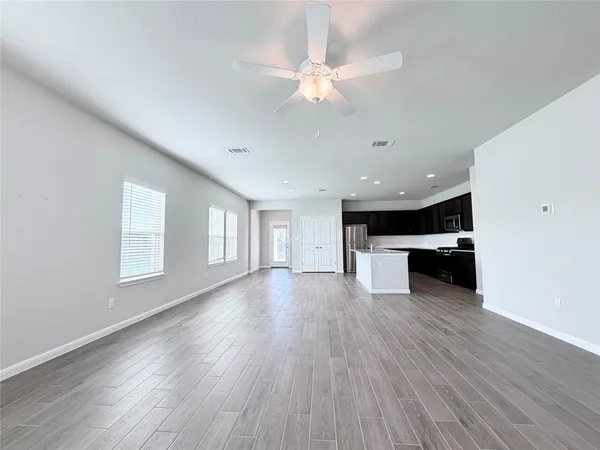 a view of an empty room with wooden floor and a kitchen