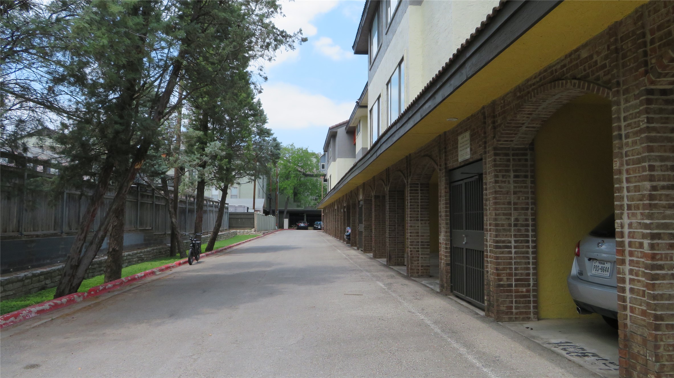 806 West 24th Street, Unit 200 Austin, TX 78705 - Photo 27 of 33 A long paved driveway leads to a series of brick archways providing covered parking below a multi-story building.