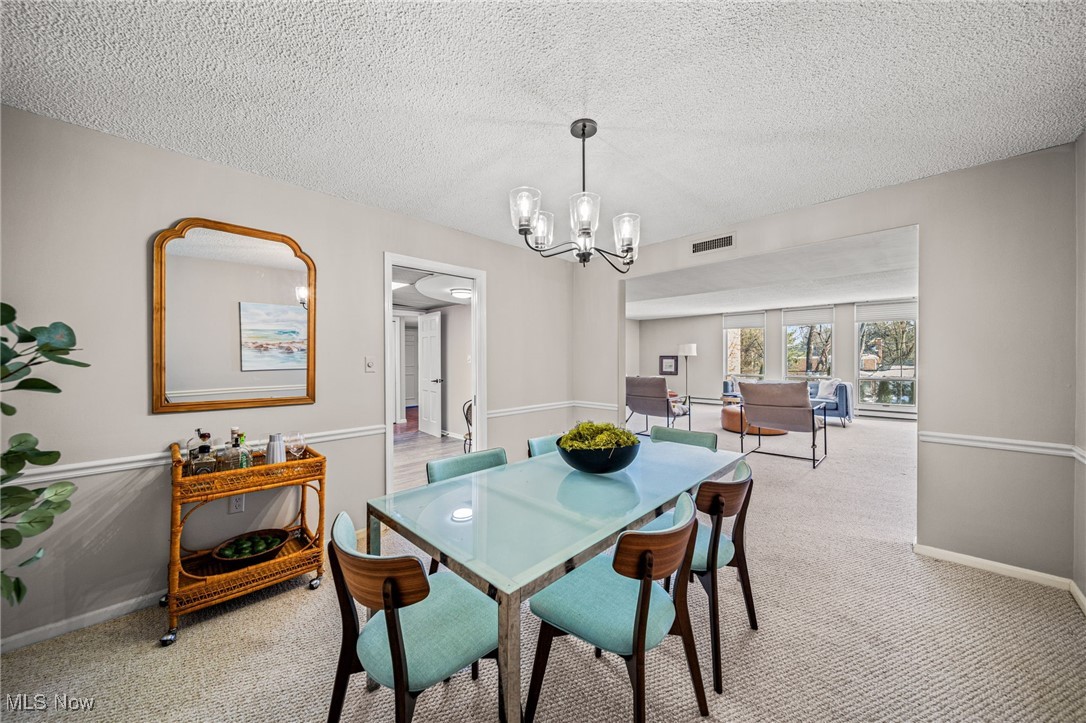 2365 Covington Road, Unit 225 Akron, OH 44313 - Photo 4 of 36 Dining space with a textured ceiling, a notable chandelier, light colored carpet, visible vents, and baseboards