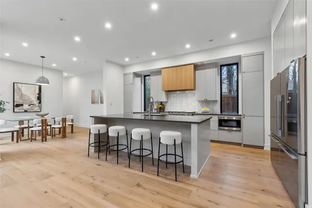 a kitchen with stainless steel appliances granite countertop a refrigerator a stove a sink a dining table and chairs with wooden floor