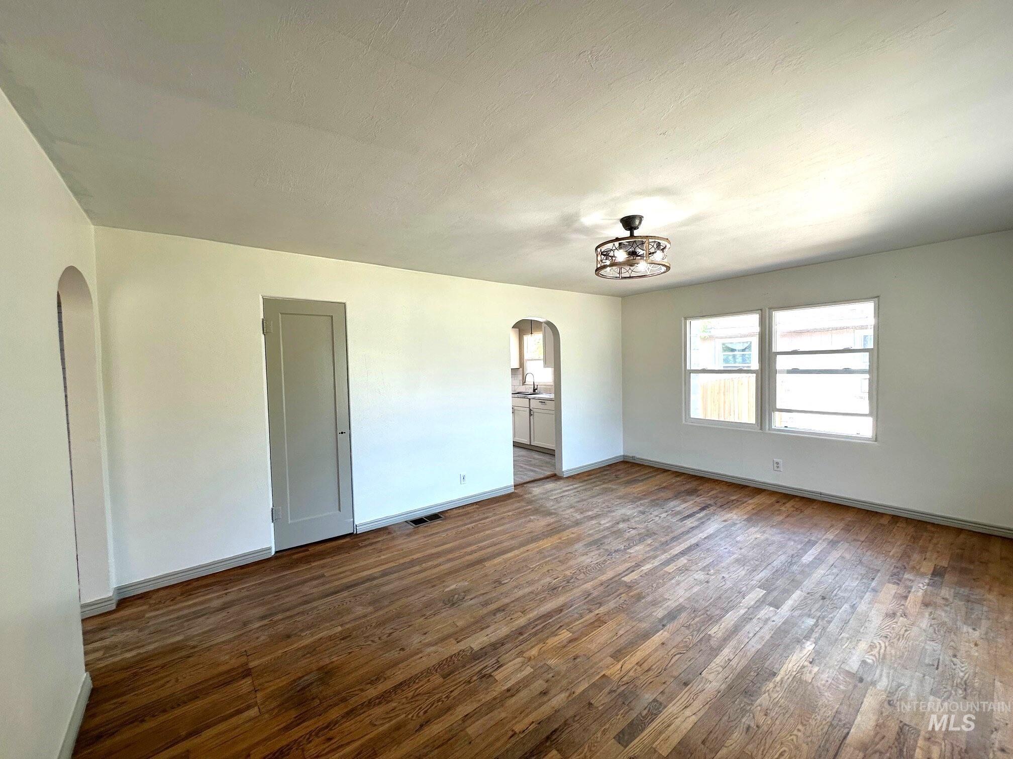 264 Southwest 10th Avenue Ontario, OR 97914 - Photo 4 of 29 Unfurnished room featuring arched walkways, dark wood-style flooring, and a chandelier