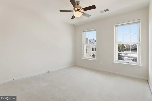 an empty room with chandelier fan and windows