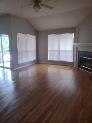 an empty room with wooden floor fire place and windows