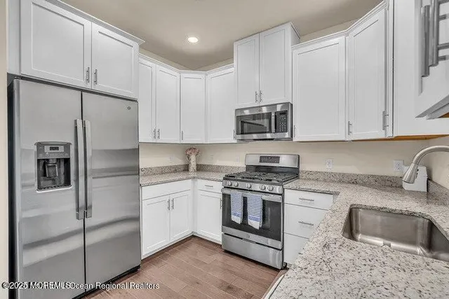 a kitchen with stainless steel appliances granite countertop a refrigerator a stove a sink and white cabinets