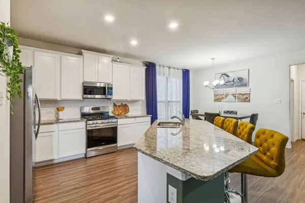 a kitchen with stainless steel appliances granite countertop a kitchen island a stove a sink a refrigerator with white cabinets and wooden floor