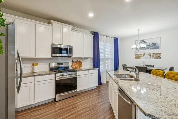 a kitchen with stainless steel appliances granite countertop a stove top oven a sink dishwasher and a refrigerator with wooden floor