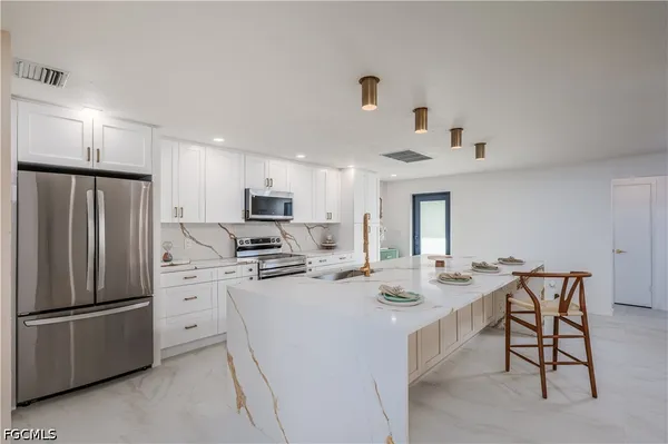 a kitchen with stainless steel appliances a stove a sink dishwasher a refrigerator and white cabinets with wooden floor